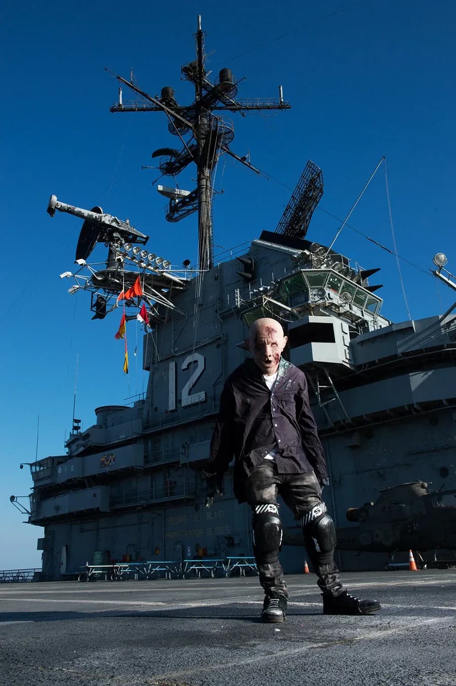 A pale, ragged figure standing on the flight deck of the USS Hornet beneath a bright blue sky.