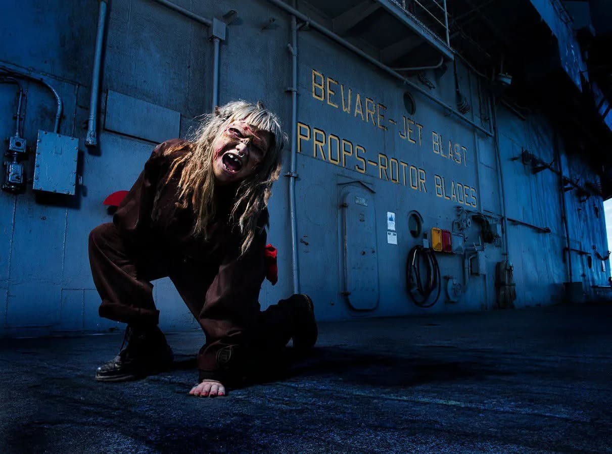 A long-haired figure crawling along an interior compartment of the ship, past a stencilled warning on the bulkhead.